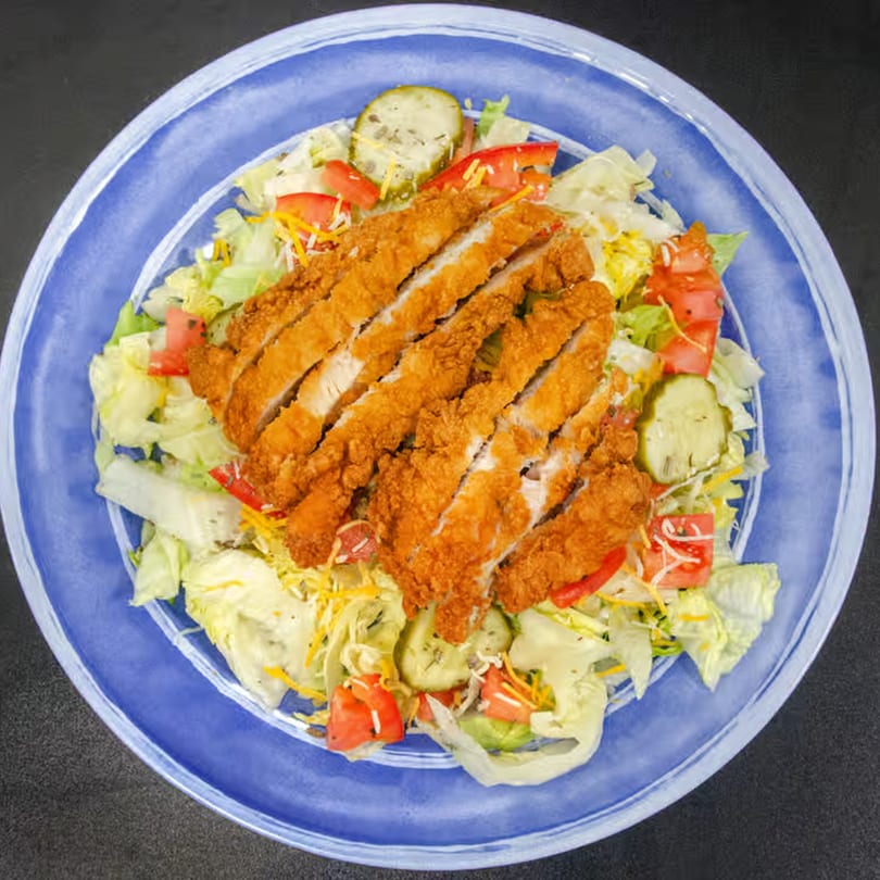 Crispy fried chicken strips on a bed of fresh lettuce, tomatoes, pickles, and shredded cheese.