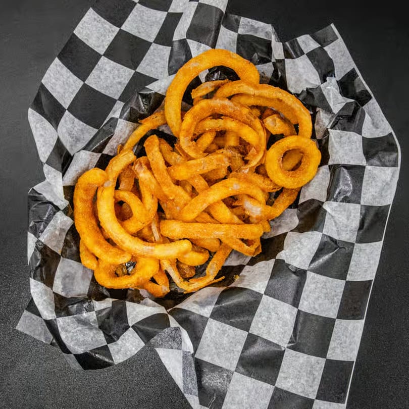 A basket of golden-brown curly fries, seasoned with spices, served in checkered paper.