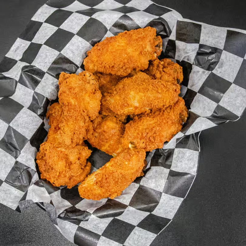 Golden-brown fried chicken wings in a black and white checkered paper-lined basket.