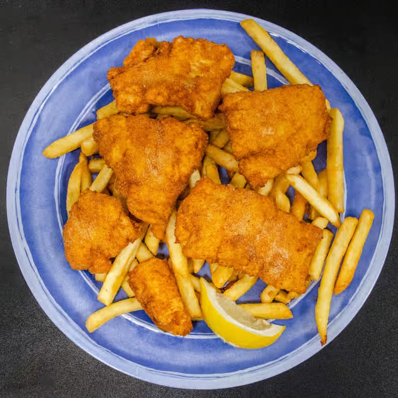 Golden-brown fried fish and french fries with a lemon wedge on a blue plate.